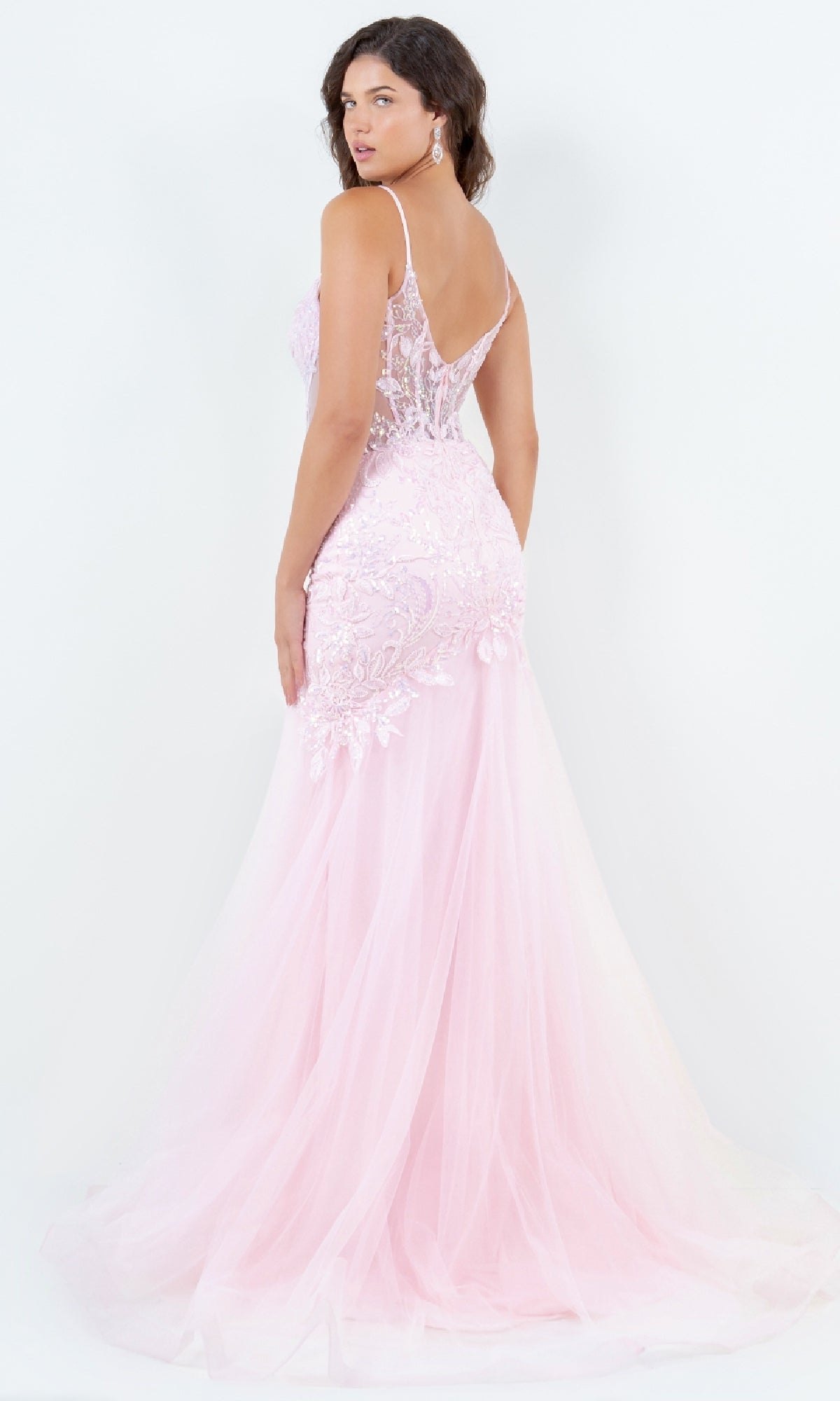 A woman stands against a white background, looking over her shoulder in the Cinderella Couture 8276J long mermaid prom dress featuring light pink lace and sheer floor-length detailing.
